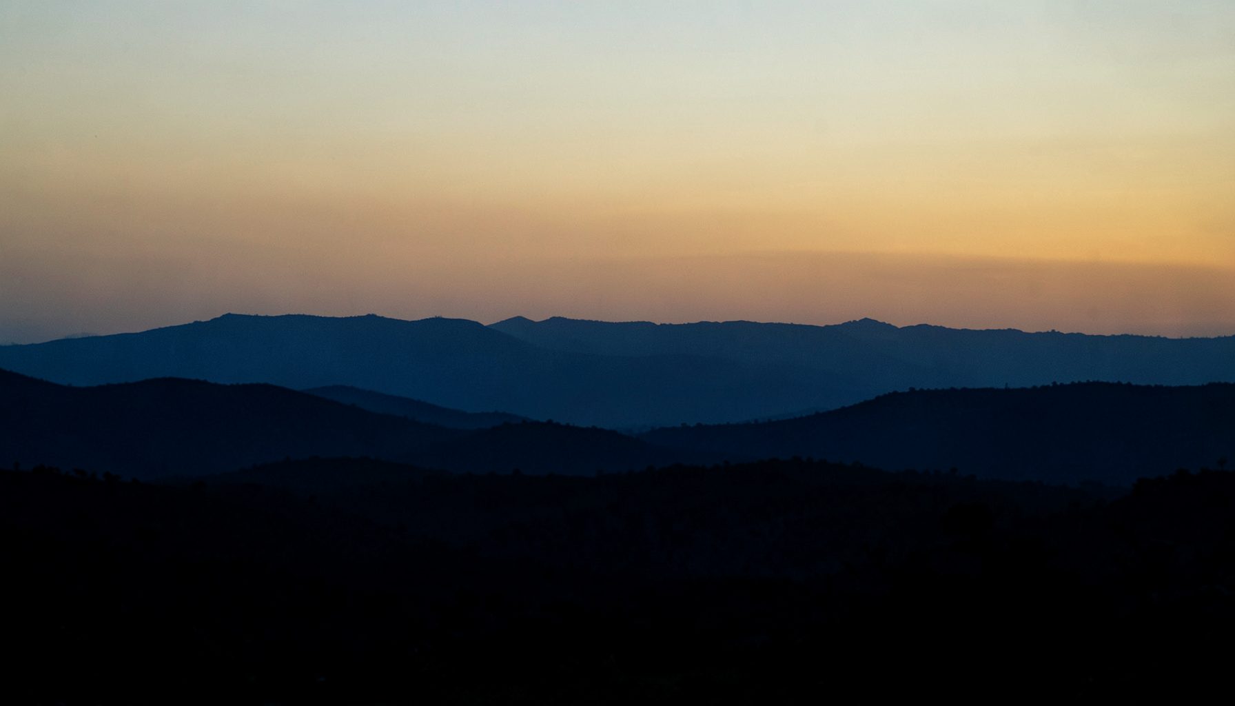Layered mountain ridges silhouetted at sunset, blue and orange gradient sky, calm mood